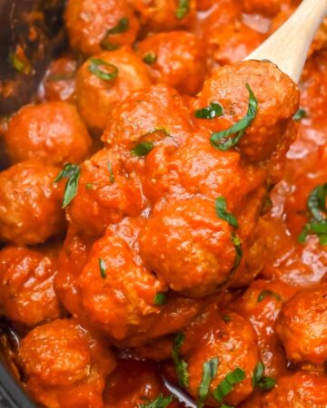 close up shot of meatballs in a crock pot with a wooden spoon.