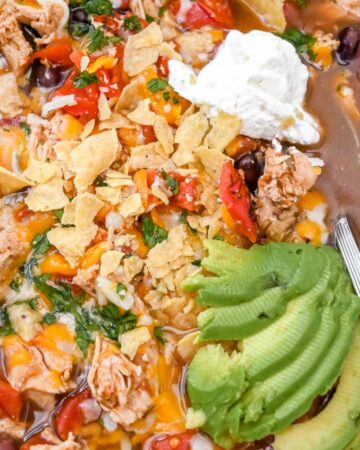 close up of 5-ingredient chicken tortilla soup topped with avocado slices and sour cream and with a silver spoon.