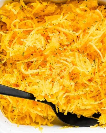 close up shot of air fryer spaghetti squash in a white casserole dish with a black spoon topped with parsley and pepper.