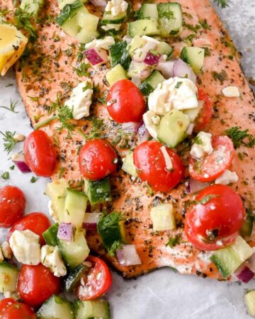 close up shot of greek salmon with cucumber tomato salad topping.